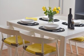 A dining table set with white plates, black placemats, and yellow napkins. There is a vase with yellow flowers and a bottle of wine on the table. - Apartment Leo (Ploce)