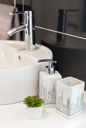 Un lavabo de salle de bain avec un robinet chromé, un distributeur de savon et deux tasses en céramique décorées de motifs représentant des paysages urbains.