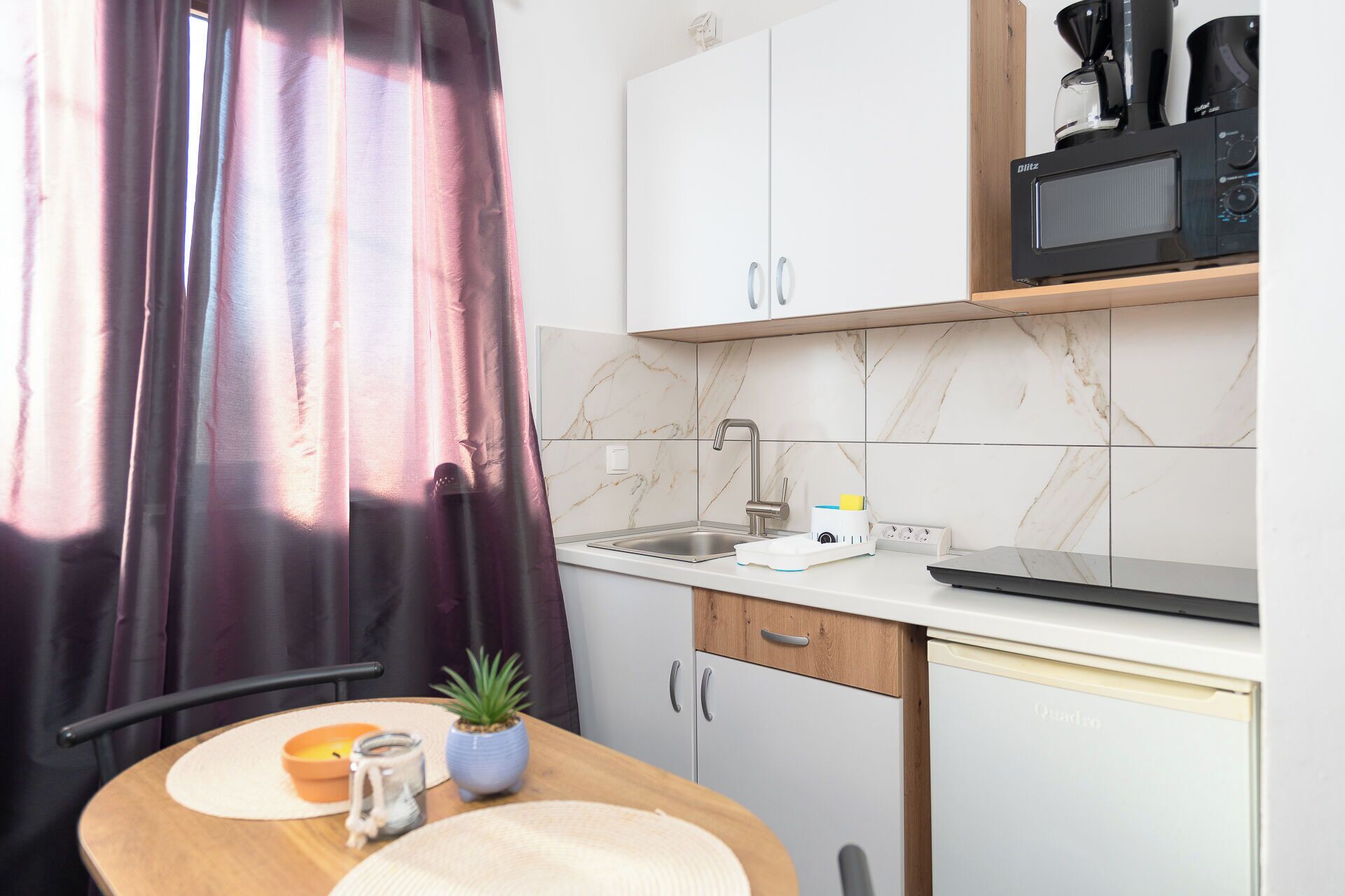 Een kleine keuken met een spoelbak, een koffiezetapparaat en kastjes.