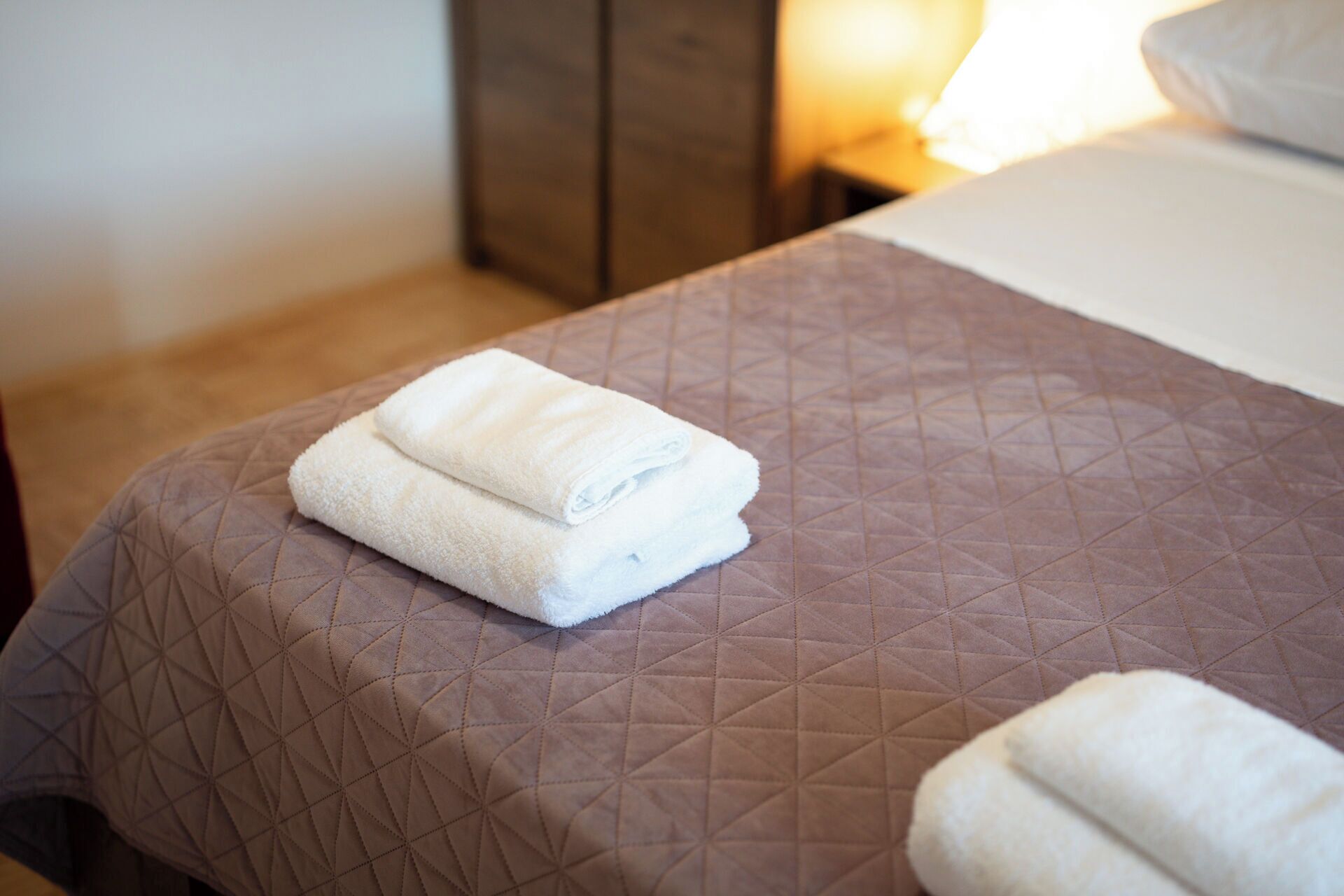 A neatly made bed with a brown quilted bedspread and two folded white towels on it.
