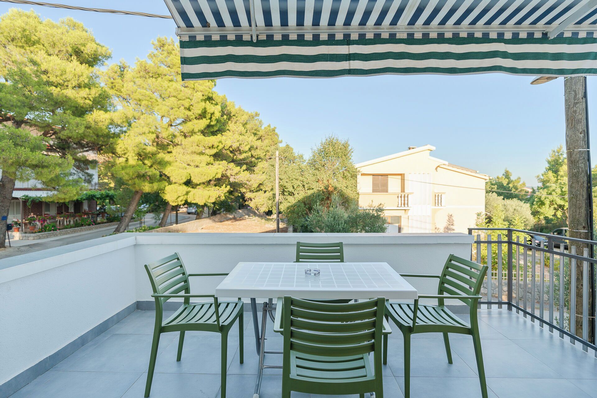 Une terrasse avec une table et quatre chaises, donnant sur un quartier résidentiel avec des arbres et un immeuble.