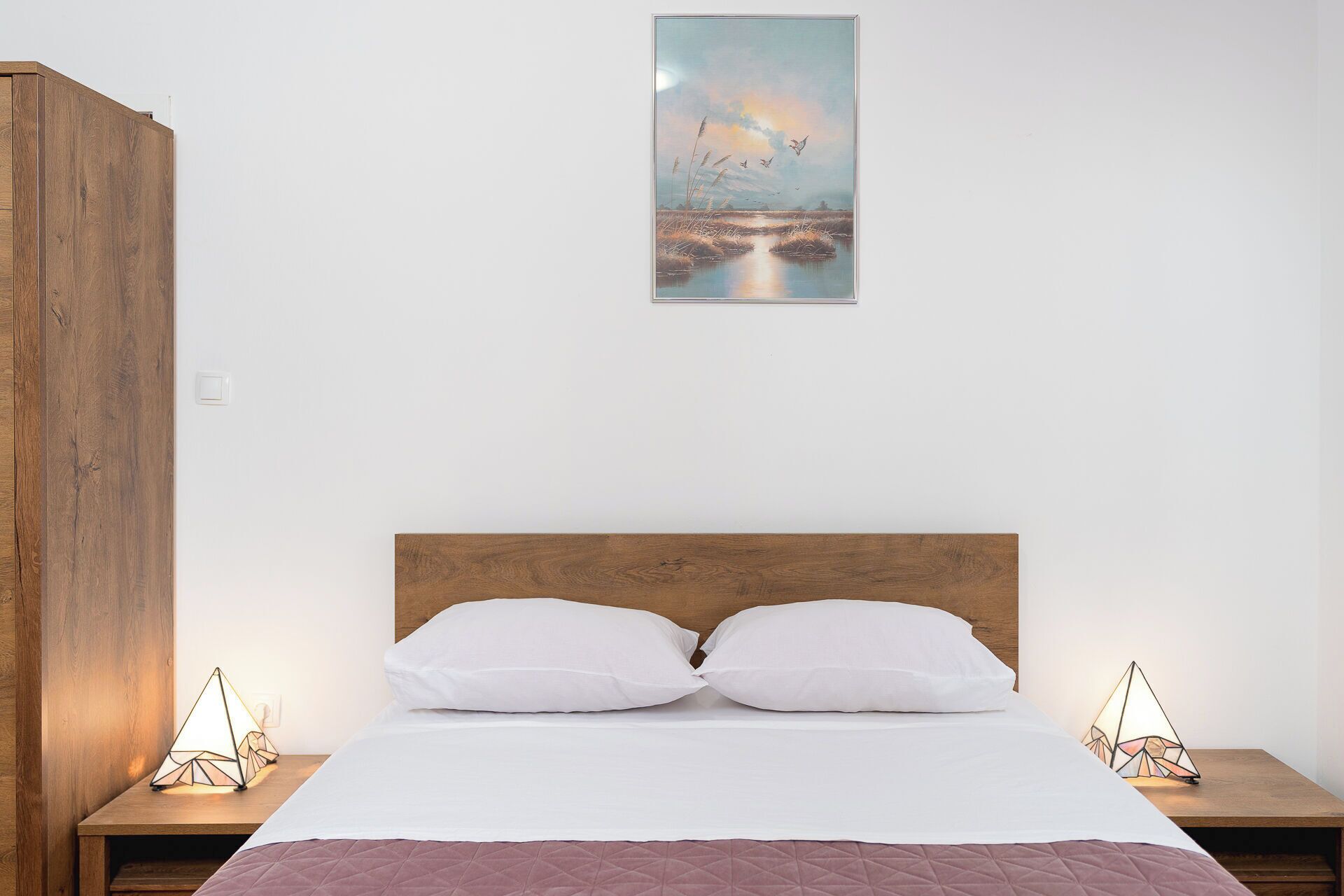 A bedroom with a wooden headboard, white bedding, and two bedside lamps.