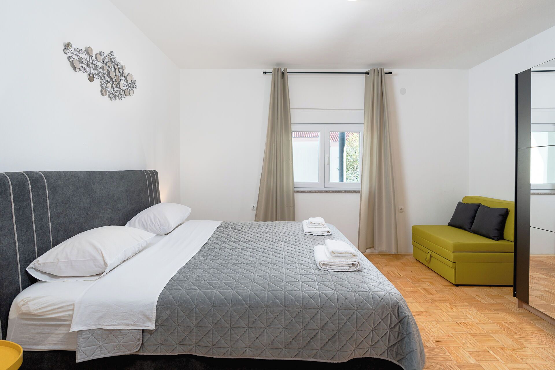 A modern bedroom with a large bed, a green sofa, and a window with curtains.