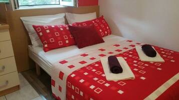 A neatly made bed with a red and white patterned bedspread, two pillows, and two rolled towels.