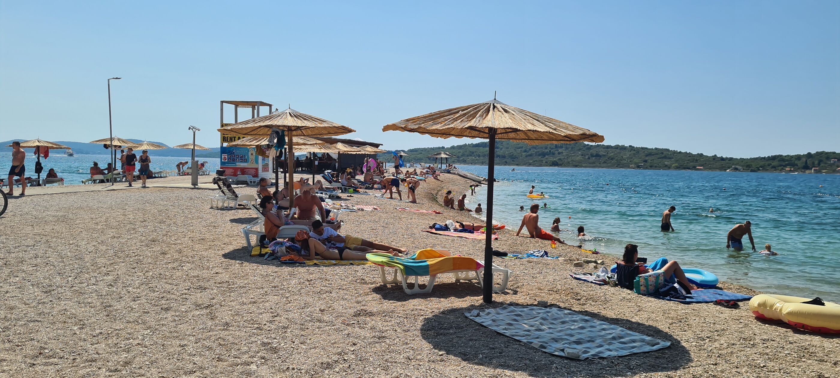 A beach with umbrellas, sun loungers, and people swimming.