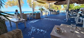 Un espacio al aire libre con mesas y sillas, vista al mar y plantas en macetas.