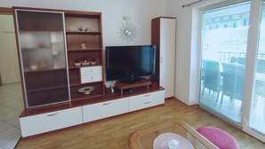 Een woonkamer met een televisie, een houten tv-meubel en een schuifdeur naar buiten.