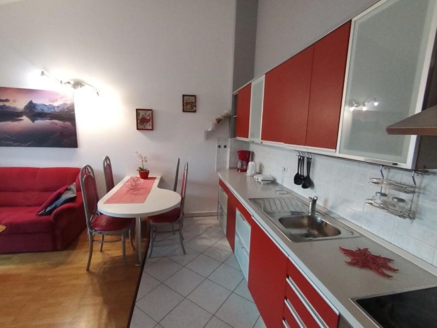 Une cuisine de taille réduite avec des meubles rouges, un plan de travail blanc et un coin repas comprenant une table et des chaises rouges.