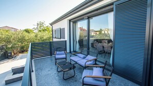Eine moderne Außenpatio mit einer Sitzecke, darunter eine Couch und Stühle, sowie eine Glastür zu einem Innenraum.