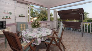 Eine überdachte Terrasse mit Tisch und Stühlen, einem Grill und Pflanzen in Töpfen an der Wand.