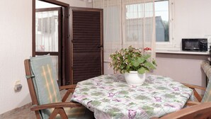 Ein Zimmer mit Holzstuhl, Tisch mit Blumenmuster bedeckter Tischdecke, Blumentopf und einem Fenster mit Vorhängen.