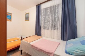 Ένα υπνοδωμάτιο με δύο κρεβάτια, ένα παράθυρο με λεπτά, διάφανα κουρτίνες και δύο φωτογραφίες σε κορνίζες στον τοίχο.
