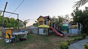 Ein Garten mit Spielhaus, Rutsche, Tisch mit Stühlen und einem Gartenbereich.