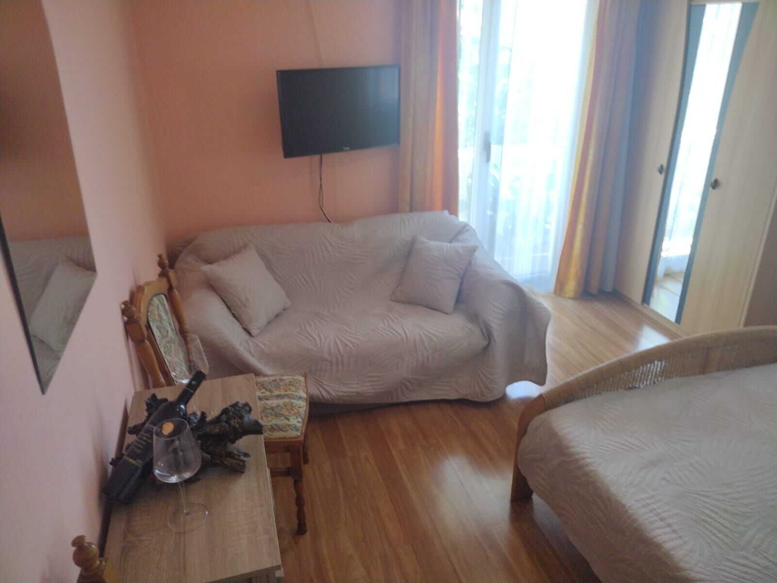A bedroom with a sofa, a small table with a wine glass, a TV mounted on the wall, and a bed.