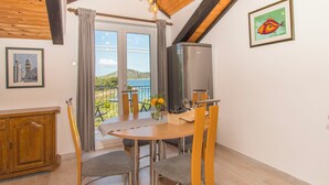 Ein Essbereich mit Holzboden, einem Tisch mit Stühlen, einem Fernseher und Meerblick durch große Fenster.