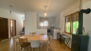 A dining area with a wooden table and chairs, a kitchen in the background, and a window with blinds. - House Katy (Ploce)