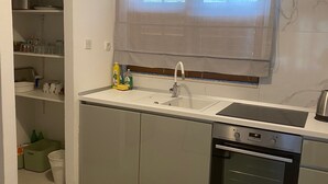 A compact kitchen with a built-in dishwasher, a stainless steel sink, and a window with blinds. - House Katy (Ploce)