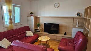 Ein Wohnzimmer mit einem roten Ledersofa, einem kleinen runden Tisch, einem Fernseher und einer Uhr an der Wand.