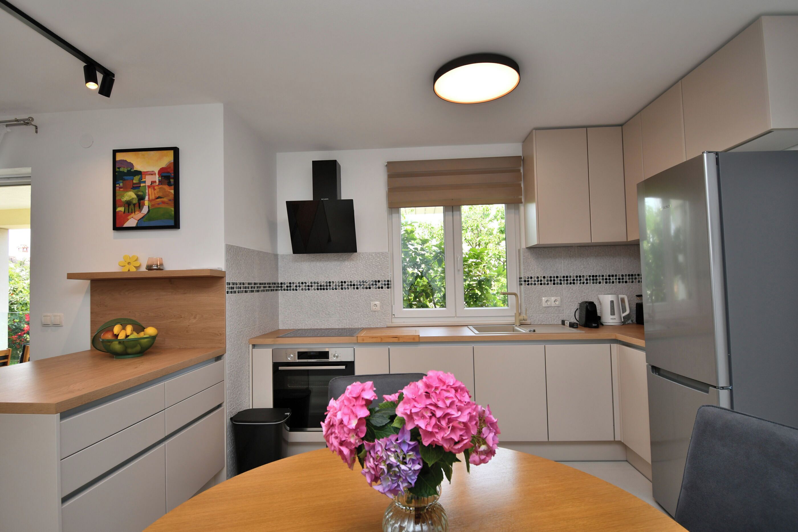 Una cocina moderna con armarios blancos, encimera de madera, refrigerador de acero inoxidable y un florero con flores sobre la mesa.