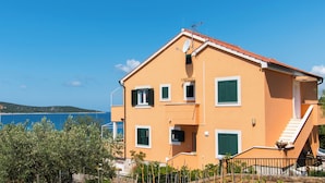 A two-story building with a red-tiled roof, green shutters, and a satellite dish. - Apartments Delfin (Vodice)