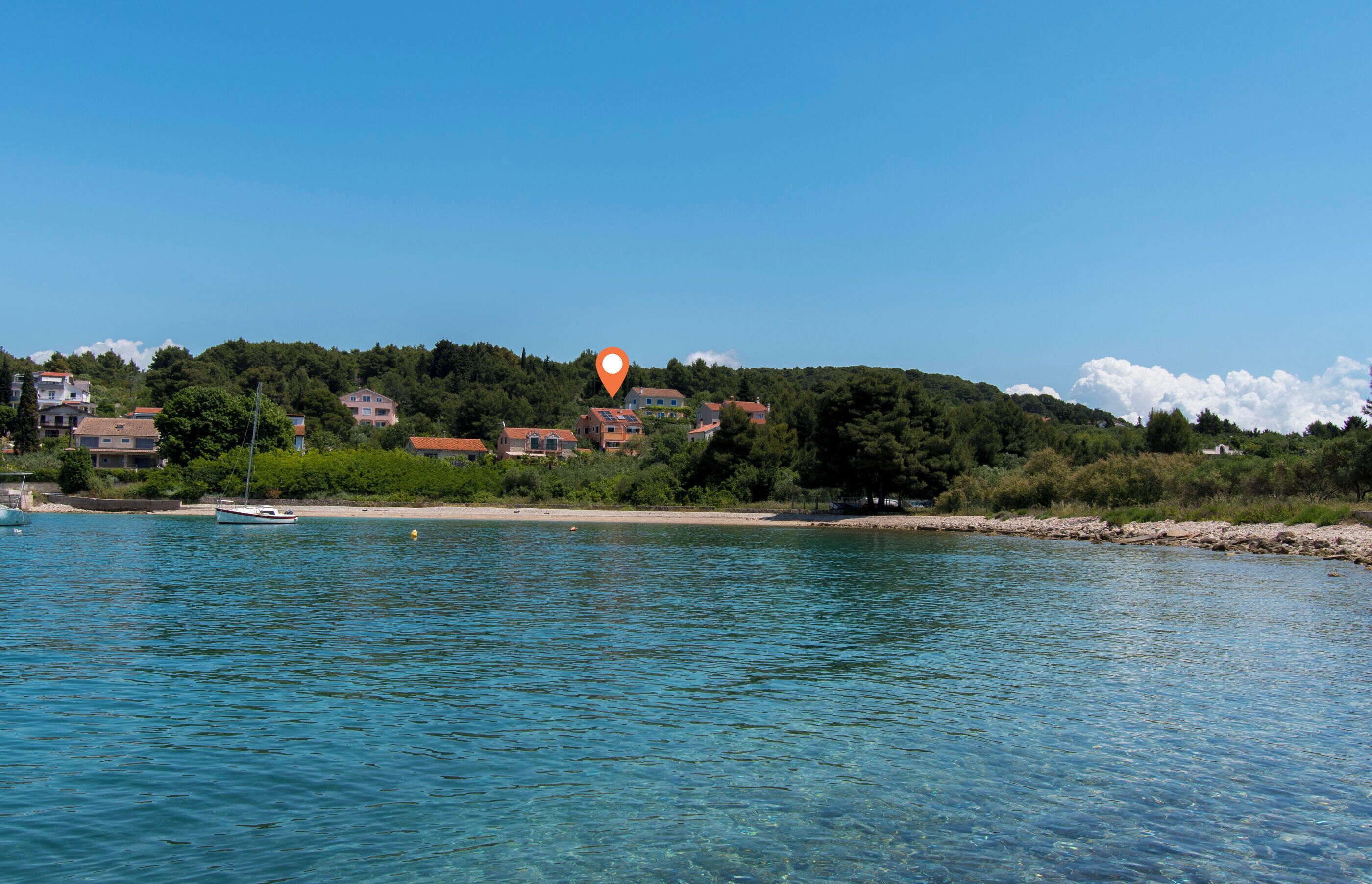 A coastal area with clear blue water, a sandy beach, and buildings on a hillside.