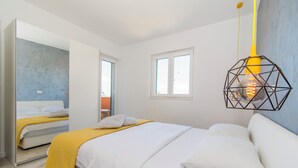 A modern bedroom with a bed, a yellow throw, a geometric light fixture, and a window. - Apartments Delfin (Vodice)