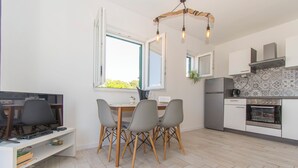 A modern kitchen with a dining area, featuring a wooden dining table, grey chairs, a built-in oven, and a large window with a view of greenery. - Apartments Delfin (Vodice)