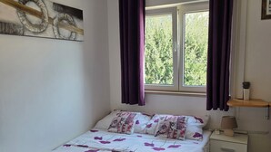 Ein Schlafzimmer mit Bett, Nachttisch, Lampe, einem Fenster mit Vorhängen und einer Wanddekoration.