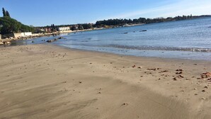 A sandy beach with scattered debris, calm water, and a distant shoreline with buildings and trees. - Room Nelly (Umag)