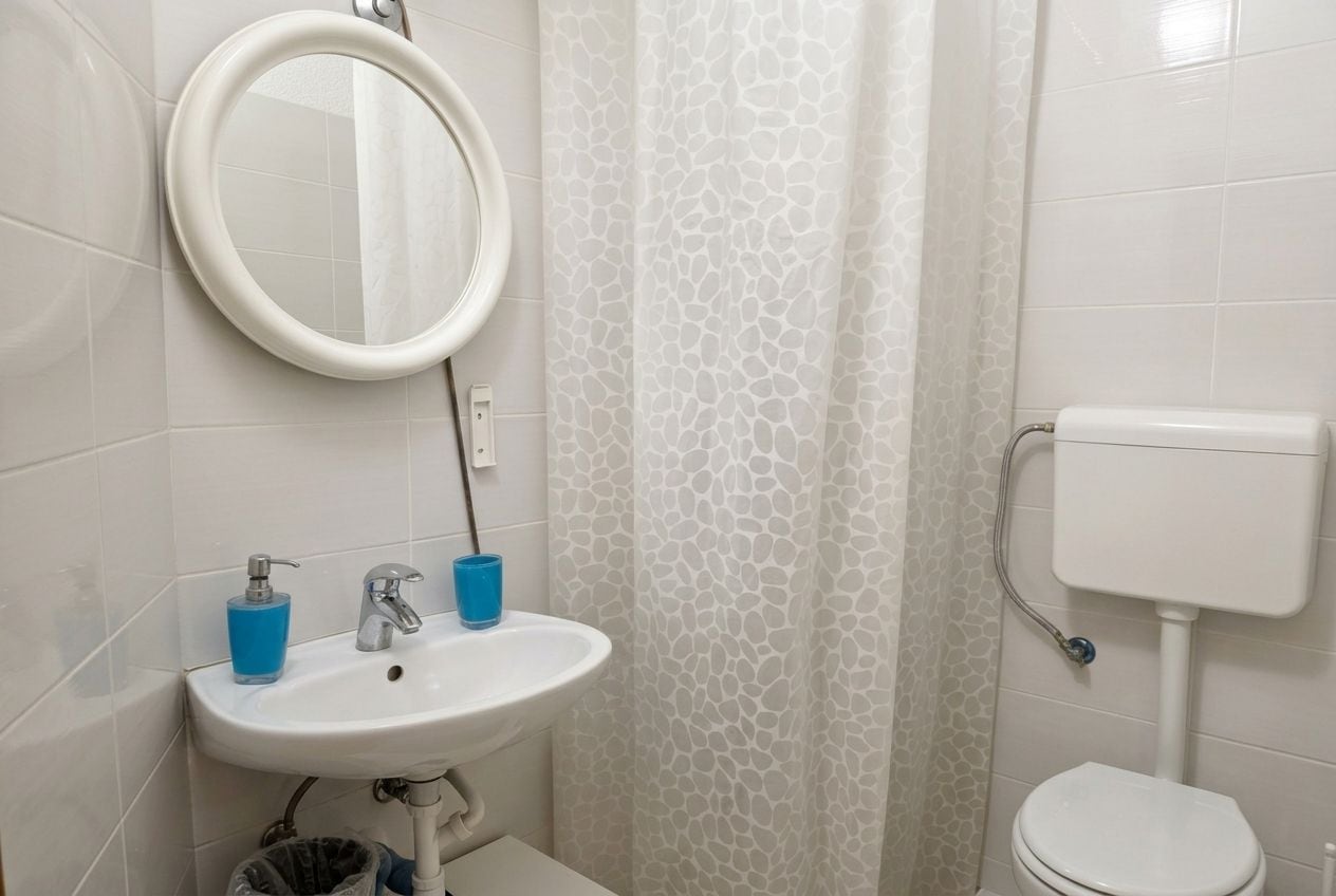 A bathroom with a white sink, a mirror, a toilet, and a shower curtain.