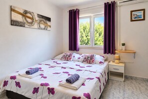 A bedroom with a bed, a nightstand, a lamp, a window with curtains, and a wall art piece. - Room Nelly (Umag)