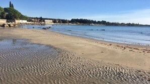 A sandy beach with gentle waves, a clear sky, and a distant shoreline with buildings. - Room Nelly (Umag)