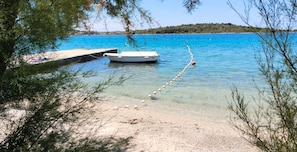 Ein unberührter Strand mit einem am Steg vertäuten Boot, umgeben von Bäumen und ruhiger See.
