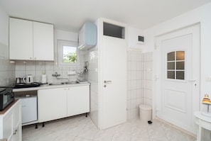 A compact kitchen with white cabinets, a microwave, a sink, and a small refrigerator. - House Garden for two (Vodice)