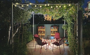 Eine Terrasse im Freien mit einem runden Tisch und Stühlen, umgeben von viel Grün und einem Holzzaun.
