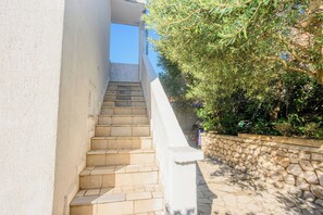 Un escalier en pierre menant vers le haut, bordé d’un mur blanc et d’un mur en pierre recouvert de verdure.