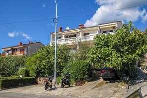 Un immeuble d’habitation doté d’un balcon, avec des motos garées devant et un ciel dégagé.
