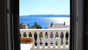 Ein Balkon mit weißer Brüstung, der auf ein Gewässer und ferne Berge blickt.