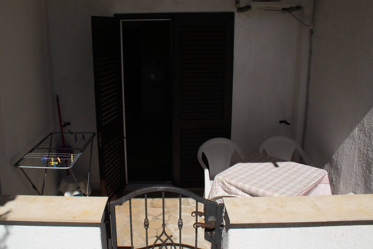 A small balcony with a metal chair and a table, a door, and a window with blinds.