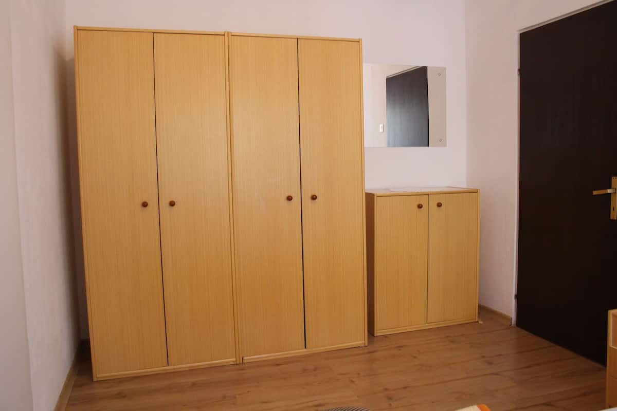 A room with a large wooden wardrobe, a small cabinet, and a mirror on the wall.