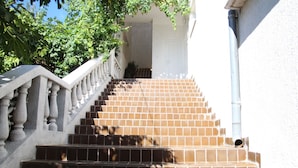 Eine Wendeltreppe mit Steinbalustrade führt zu einer Tür, umgeben von Grünpflanzen.