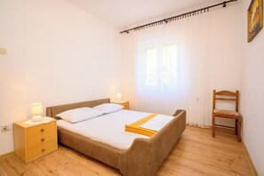 A bedroom with a bed, bedside tables, a chair, and a window with curtains. - Apartments Marija (Novi Vinodolski)