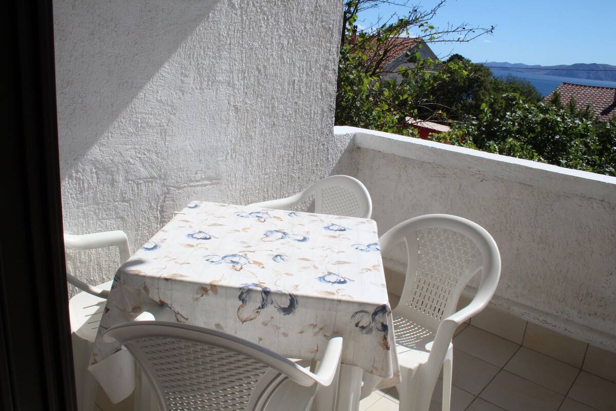 A balcony with a table and chairs, a view of the sea, and a building in the background.