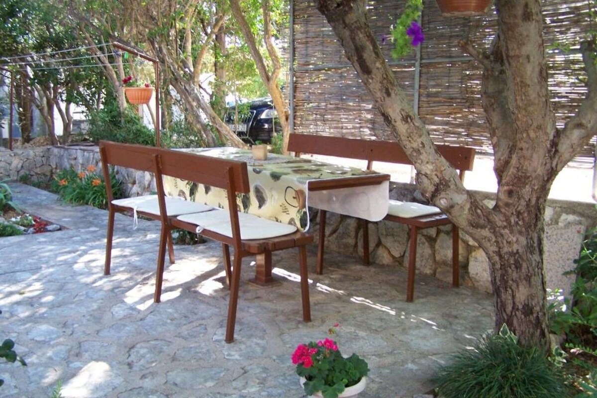 Eine Terrasse im Freien mit Steinboden, Holzmöbeln und Blumentöpfen.