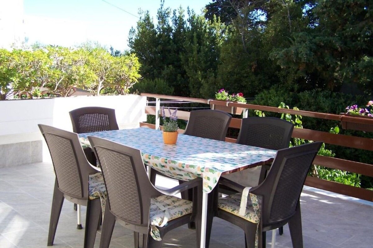 Eine Terrasse im Freien mit Tisch und Stühlen, umgeben von einem Holzzaun und viel Grün.