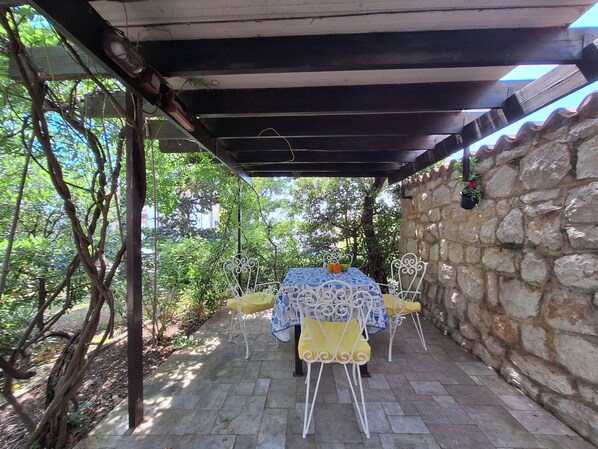 Un patio abrité, doté d’une table et de chaises, entouré de murs en pierre et de verdure.