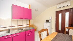 Una cocina compacta con gabinetes rosados, una mesa de comedor de madera y un refrigerador blanco.
