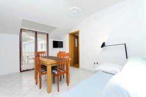 A bedroom with a bed, a desk with chairs, a television, and a door leading to another room. - Apartments Josip (Vodice)