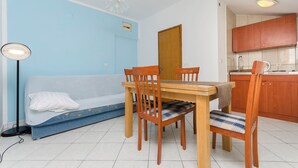 Un espacio habitable compacto con una mesa y sillas, un sofá, una kitchenette y un ventanal pequeño.