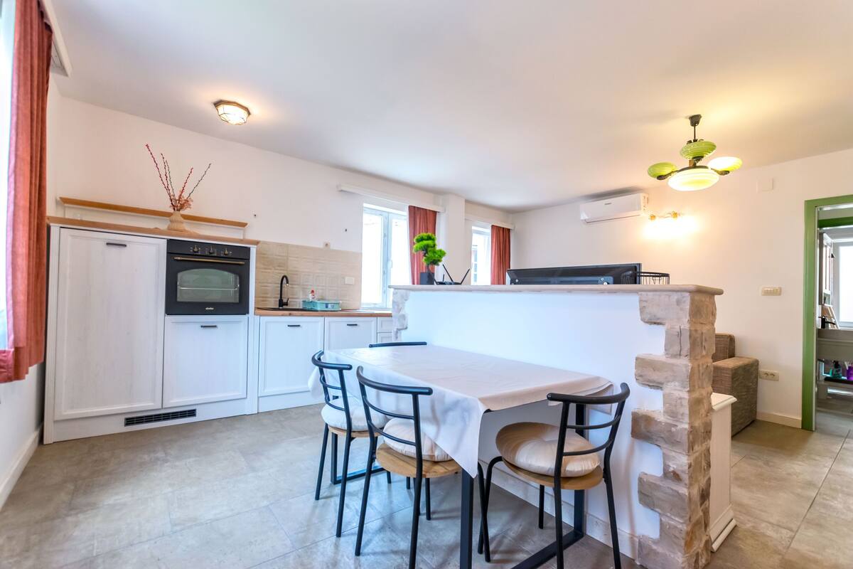 A modern kitchen with white cabinets, a dining table with four chairs, and a stone accent wall.